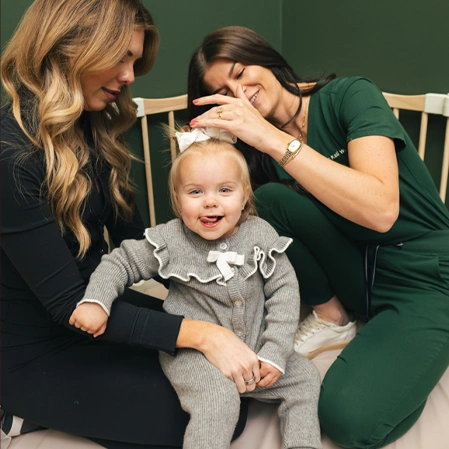 Adult in green scrubs gently adjusting a toddler’s head